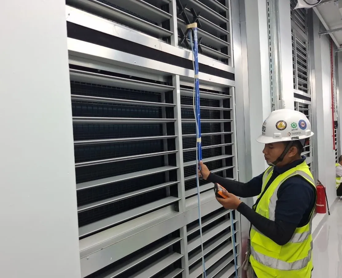 A Pariksa technician holding an airflow probe against a louver bank and reading the meter.